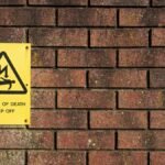 A bold warning sign on a brick wall displaying 'Danger of Death', emphasizing caution.