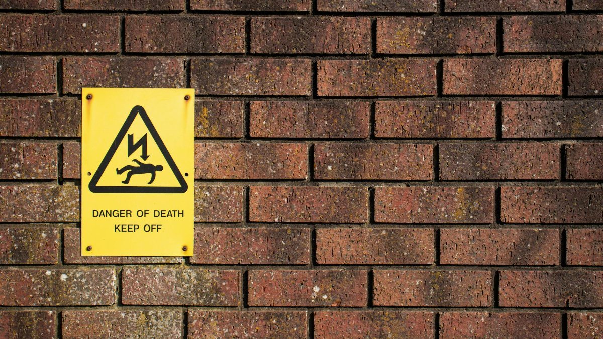 A bold warning sign on a brick wall displaying 'Danger of Death', emphasizing caution.