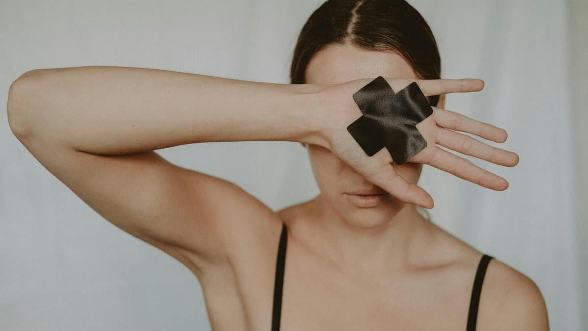 Faceless young lady in black underwear showing hand with black cross tape against abuse on white background