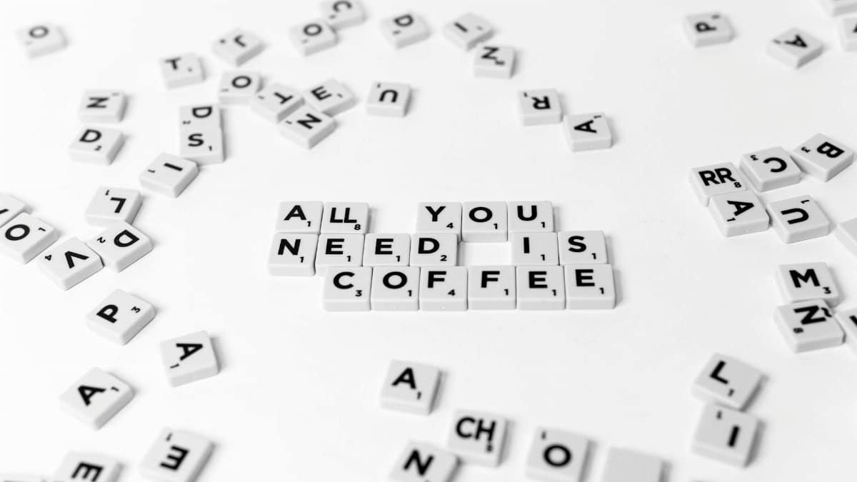 Scrabble tiles spell out 'All You Need Is Coffee' on a white background, offering a creative still life.