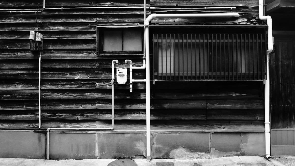 Grayscale image of a rustic wall with exposed pipes, depicting vintage urban architecture.