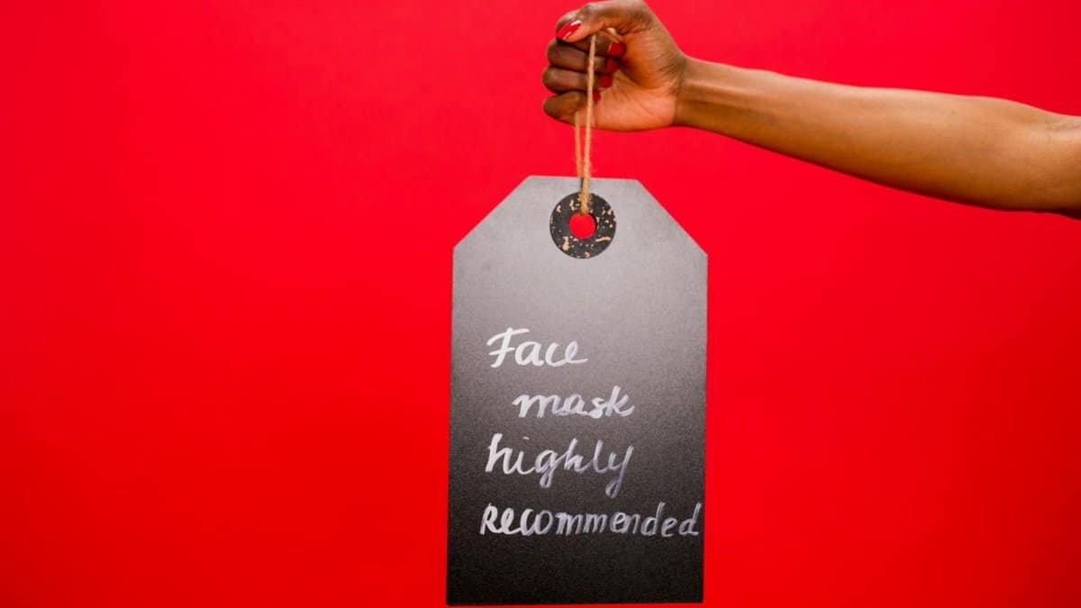 A hand holding a sign reading 'Face mask highly recommended' against a red background.