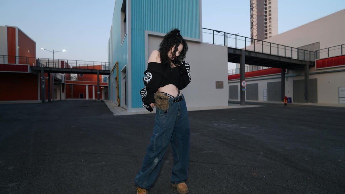 A stylish woman poses in an urban setting with colorful modern architecture.