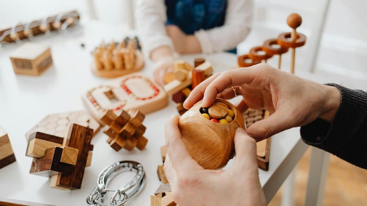 Close-up of hands engaging with wooden brain teasers on a table indoors.
