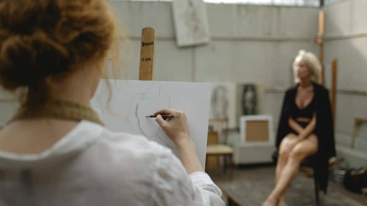 An artist sketches a model posing in an indoor art studio, showcasing creativity and focus.