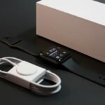 A modern smartwatch with charger displayed elegantly alongside its packaging on a dark surface.