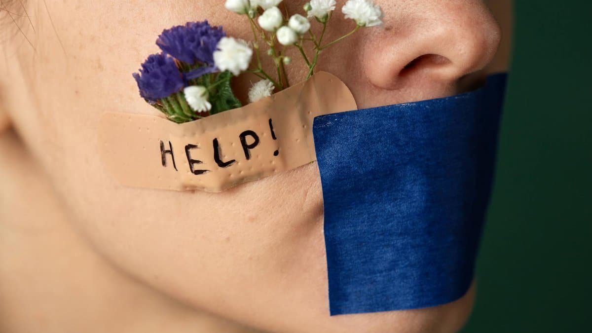 A conceptual image featuring flowers and tape on a face symbolizing silence and a cry for help.