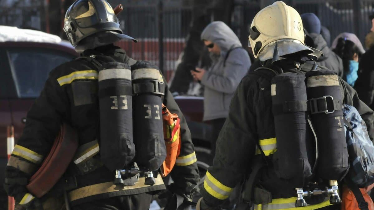 Two firefighters in full gear walking through an urban area.