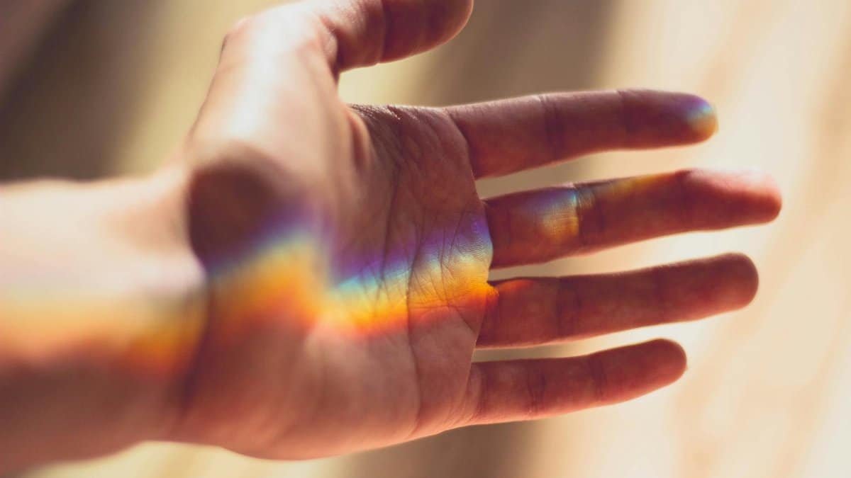 A hand with a beautiful rainbow light refraction across the palm.