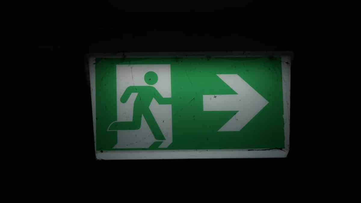 Illuminated green emergency exit sign with an arrow pointing right in a dark setting.