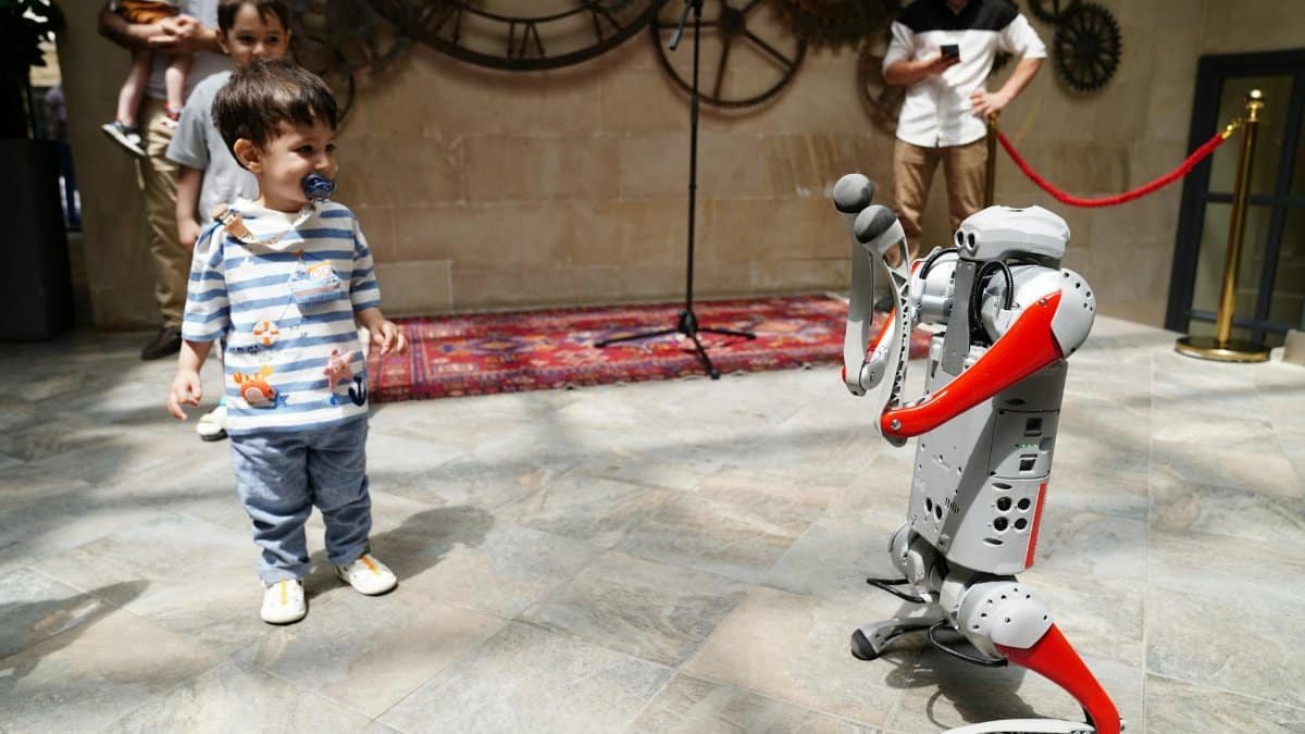 A young boy engages with a humanoid robot during an indoor tech exhibition, symbolizing future innovation.