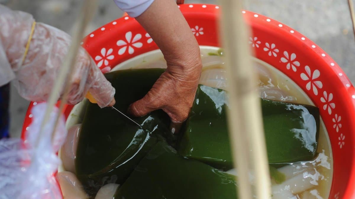 Street vendor prepares green gelatin dessert in colorful bowl illustrating traditional street food culture.