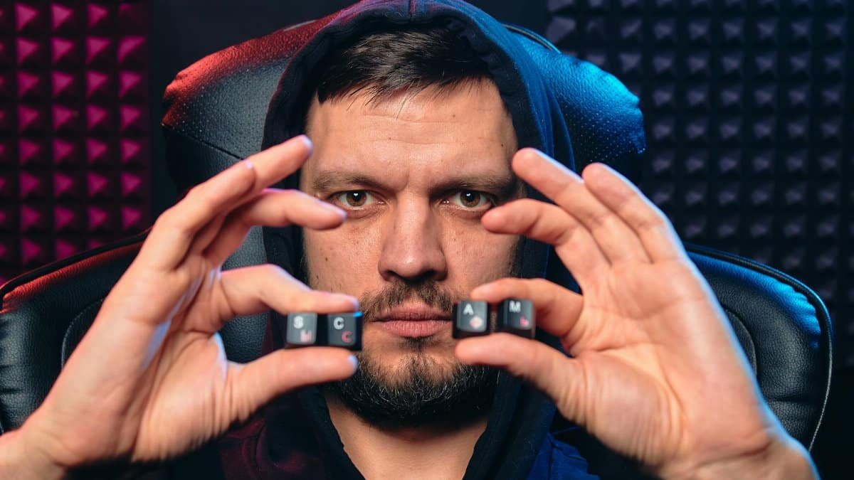 Man in hoodie holding alphabet keys spelling 'SCAM', symbolizing cybersecurity threat.