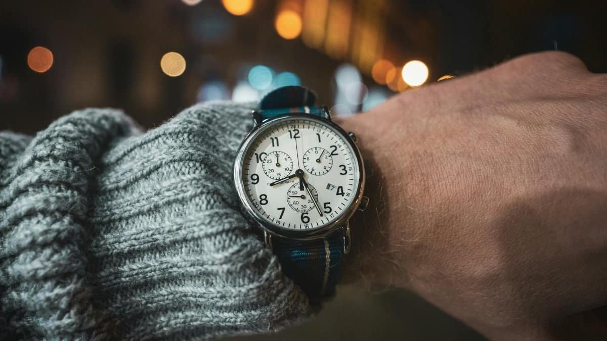 A detailed close-up of an analog wristwatch on a wrist in a night setting with bokeh background.
