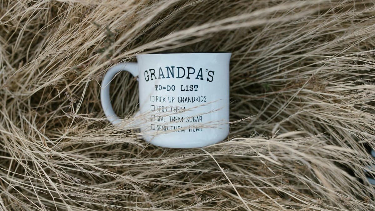 A playful Grandpa's to-do list mug nestled in dry grass, perfect for gifting a grandfather.