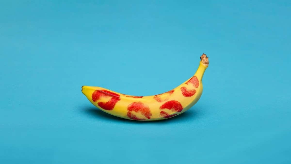 A vibrant studio shot of a banana covered in red lipstick kiss marks against a blue background.