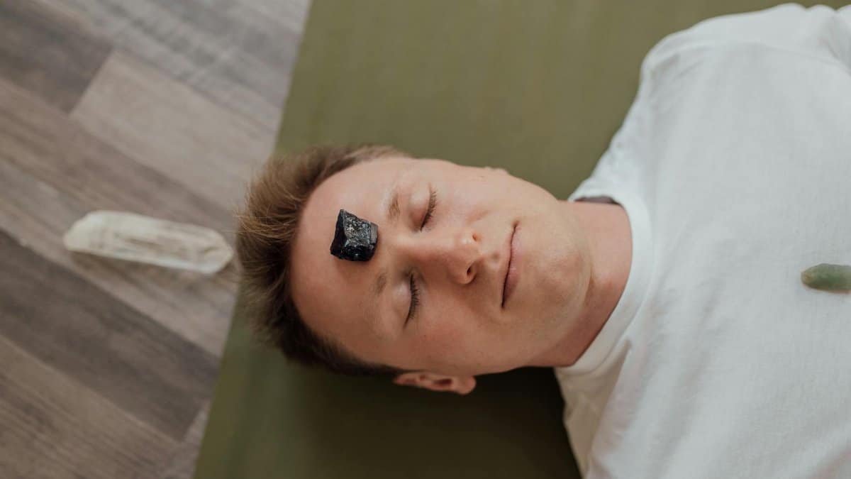 A man lying down with a healing crystal on his forehead for relaxation and wellbeing.