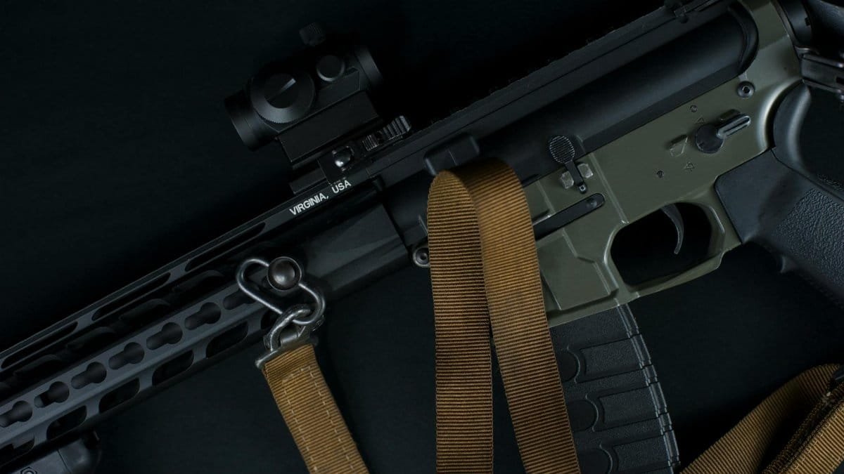 High-angled shot of a modern tactical rifle featuring a mounted sight and sling, highlighted on a dark background.