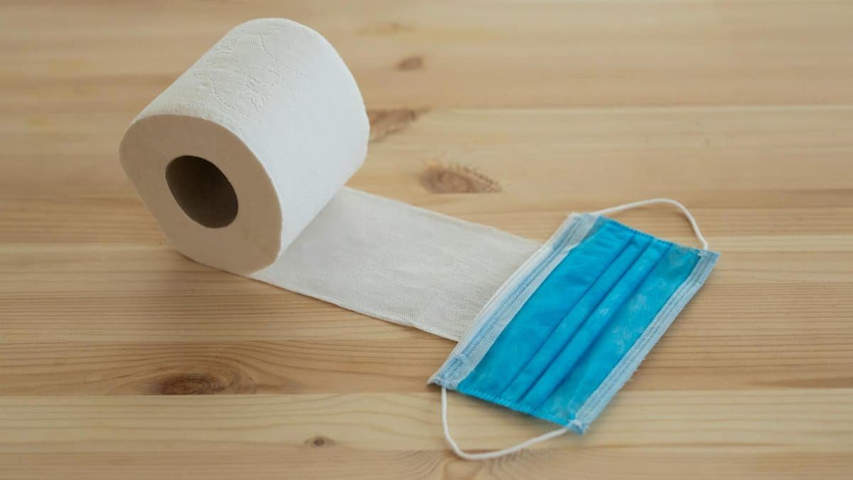 A rolled toilet paper next to a face mask on a wooden table, symbolizing hygiene and safety during a pandemic.