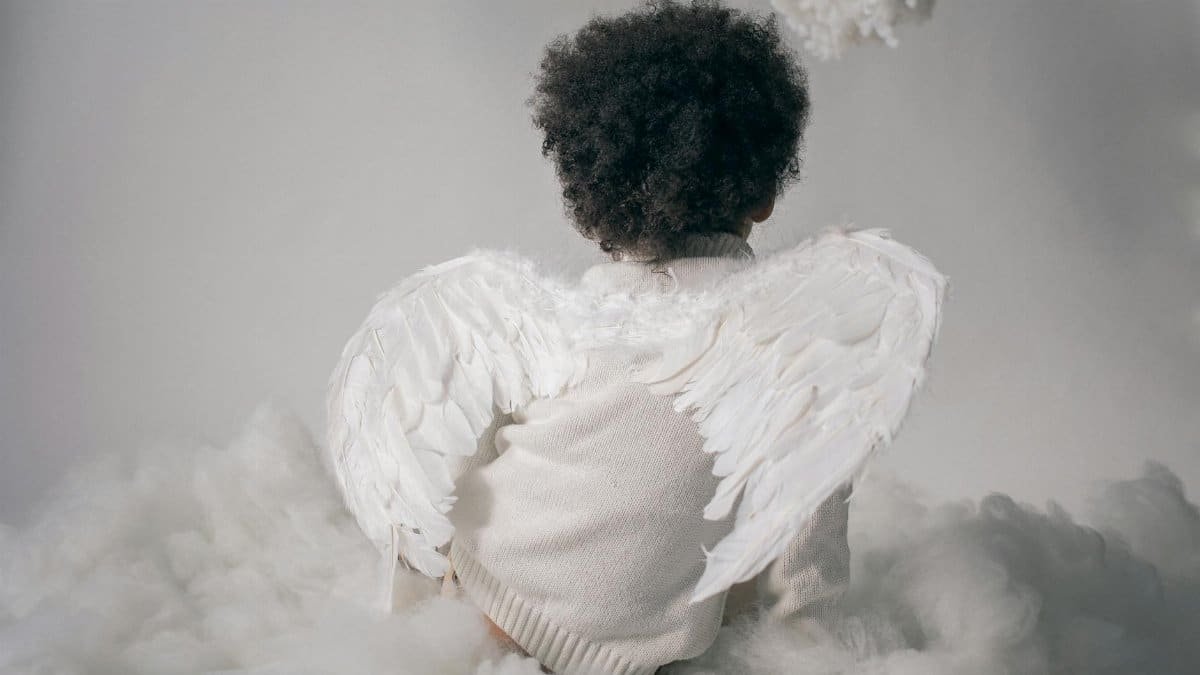 A child wearing angel wings surrounded by cloud-like props in a studio setting.