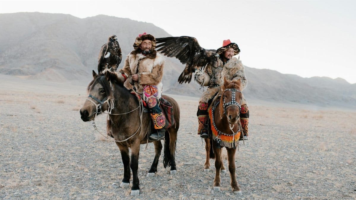 Mongolian eagle hunters on horseback in traditional attire, showcasing vibrant culture.