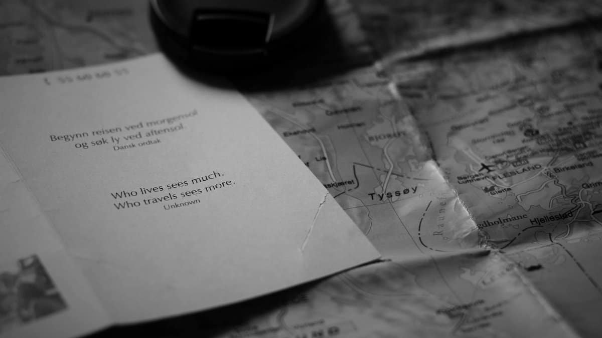 A black and white image of an inspirational travel quote alongside a map and camera lens cap.