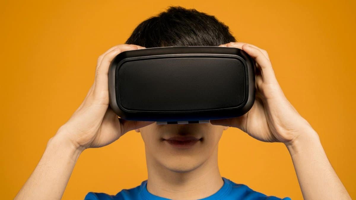 Young man with VR headset on orange background, fully immersed in virtual reality.