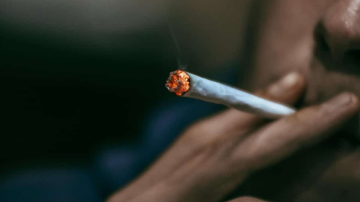 A detailed close-up of a hand holding a burning cigarette, emphasizing smoking habit.