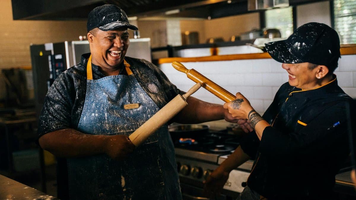 Two chefs having fun in a restaurant kitchen with rolling pins.