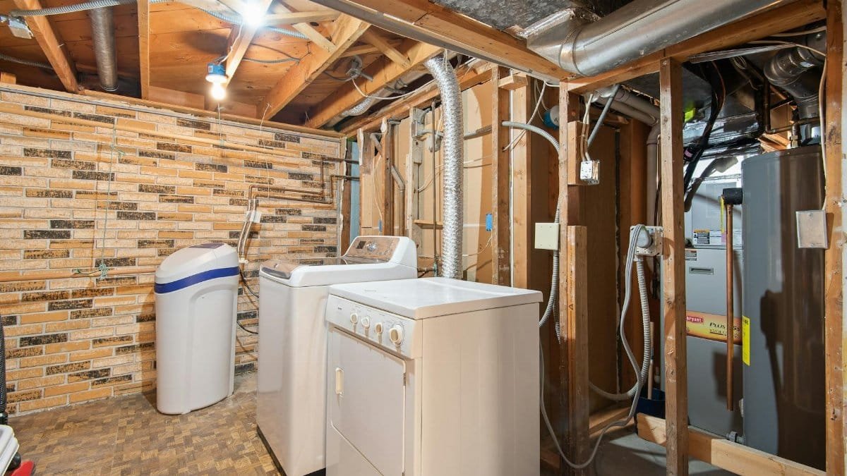 Spacious basement laundry room featuring modern appliances and exposed brickwork.