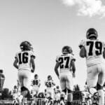 Black and white image of high school football players running onto the field in a dynamic display of sports action.