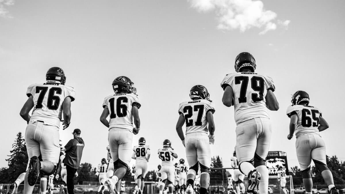 Black and white image of high school football players running onto the field in a dynamic display of sports action.