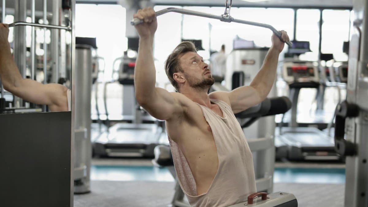 Man exercising on a lat pull-down machine in a modern gym setting.