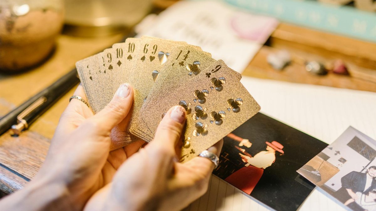 Hands holding playing cards on a desk with photos and crystals, suggesting card magic or divination.