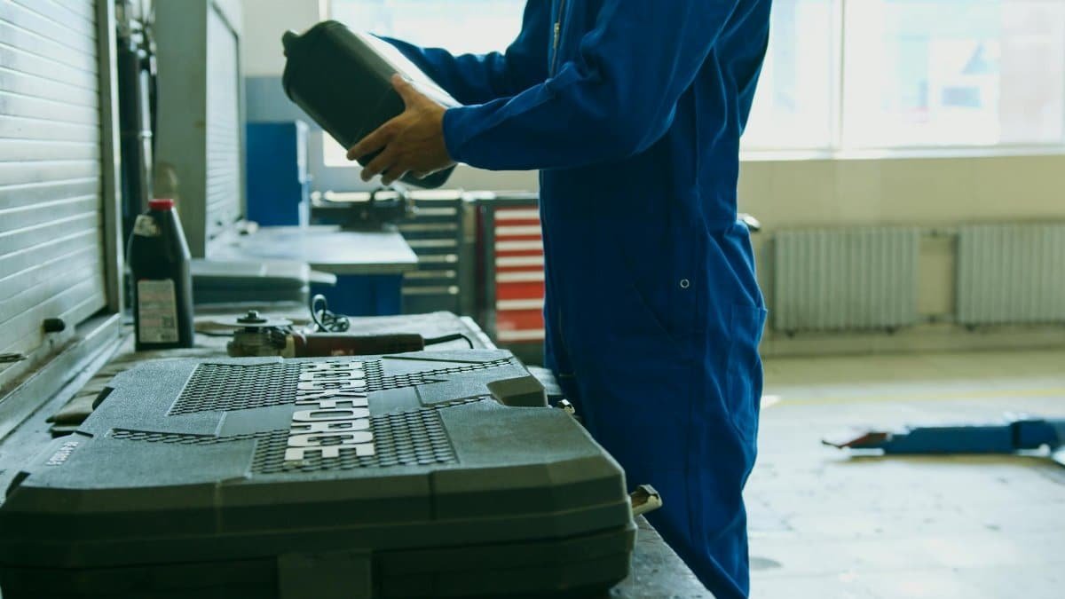Mechanic in blue overalls holding engine oil container in a workshop environment, enhancing maintenance efficiency.