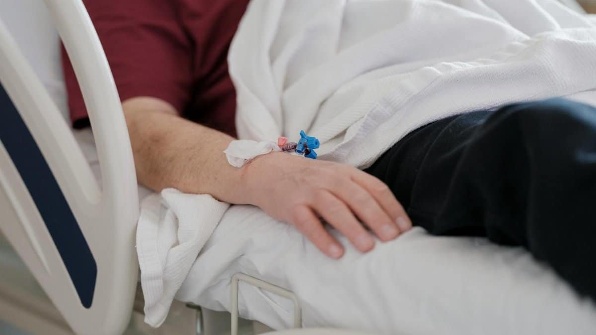 Close-up of a patient's hand with an IV drip lying on a hospital bed.