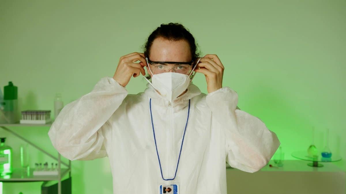 Scientist wearing protective gear in a laboratory with green lighting.