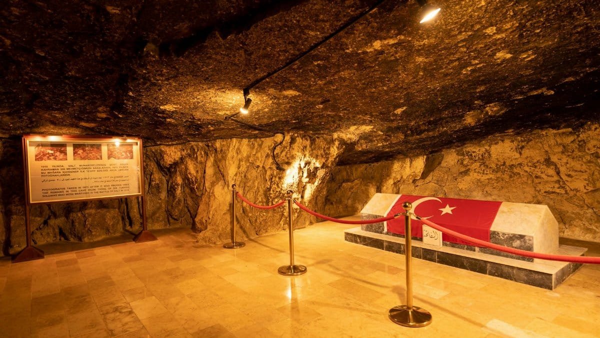 An underground tomb with a Turkish flag inside a rocky cave illuminated with warm lighting.