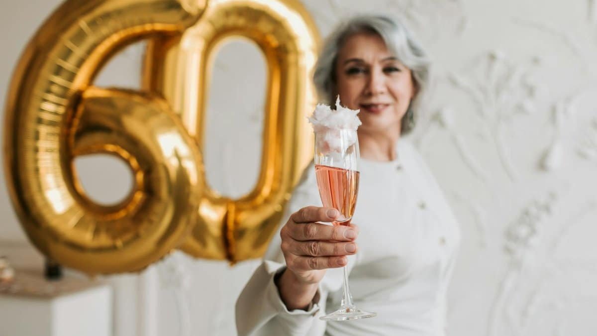 Senior woman celebrating 60th birthday holding champagne in elegant setting.