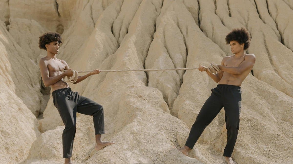 Two shirtless men engage in a tug of war on rocky desert terrain, showcasing strength.