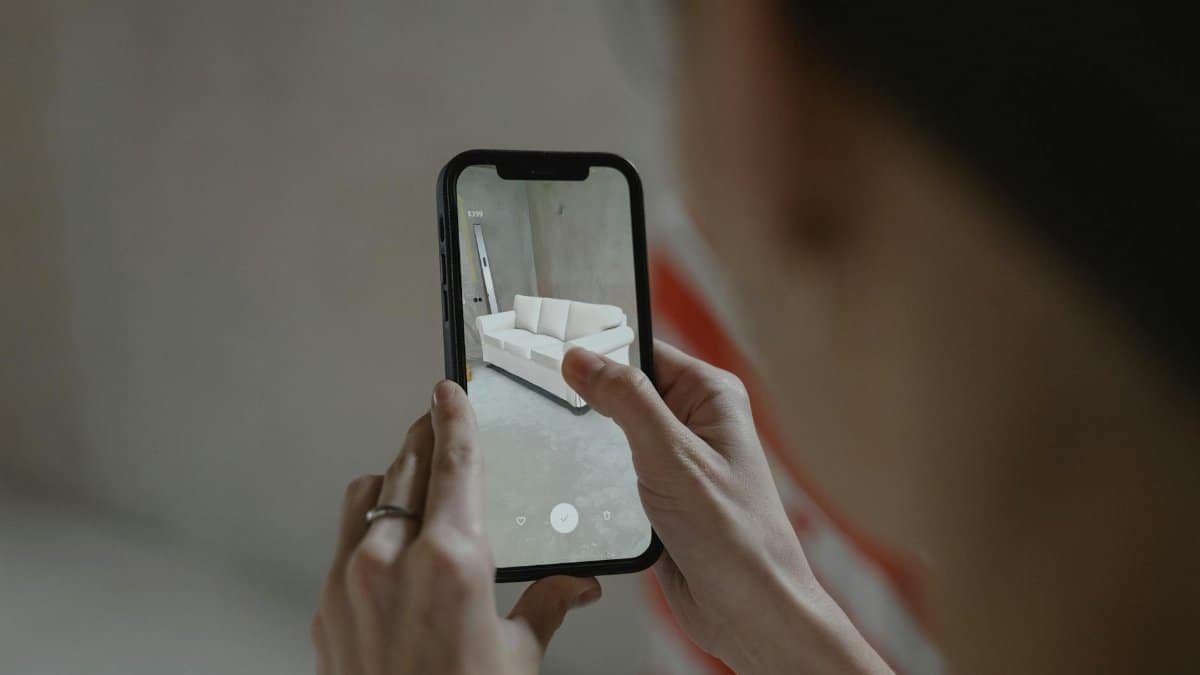 Person using augmented reality on smartphone to visualize a sofa in a room.