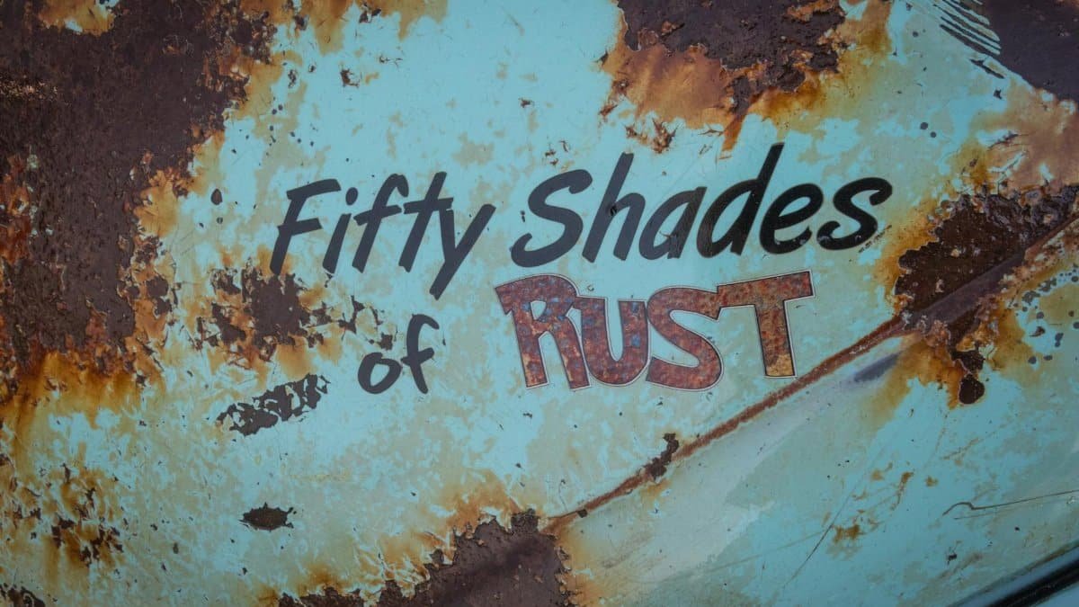 Close-up of a rusty metal surface with humorous text, highlighting corrosion and decay.