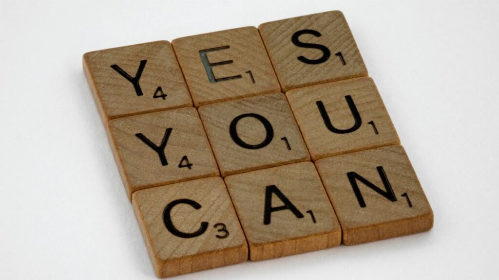 Wooden Scrabble tiles on white surface spelling 'Yes You Can,' promoting positivity and motivation.