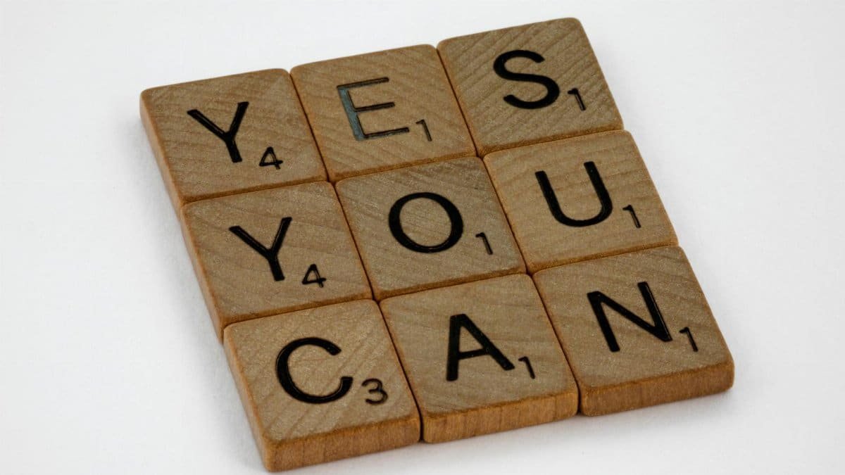 Wooden Scrabble tiles on white surface spelling 'Yes You Can,' promoting positivity and motivation.