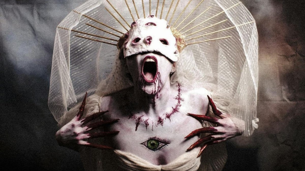 Gothic woman with a haunting costume, veil, and painted mask in an artistic horror portrait.