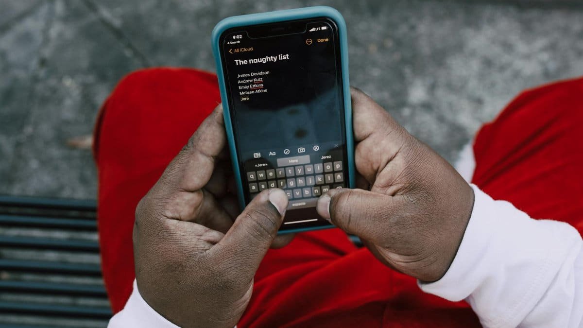 Close-up of hands typing a 'naughty list' on a smartphone outdoors.