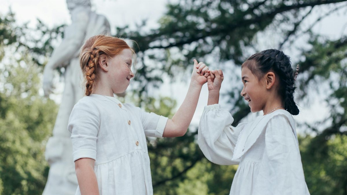 Two smiling girls making a pinky promise outdoors, surrounded by greenery.