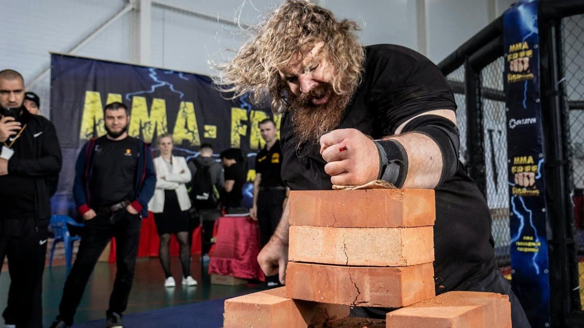 A strongman breaks bricks in an impressive display of power during a competition indoors.