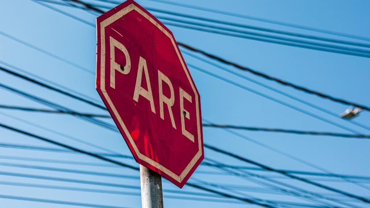 Red stop sign with 'PARE' text against a clear blue sky and overhead power lines.