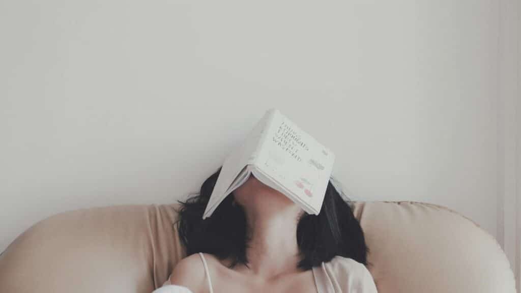 A woman relaxes indoors with an open book resting on her face, enjoying a tranquil moment.